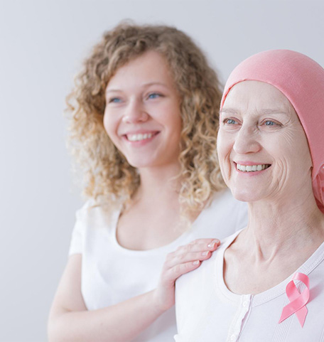Dochter en moeder met borstkanker glimlachen tegen een witte achtergrond.